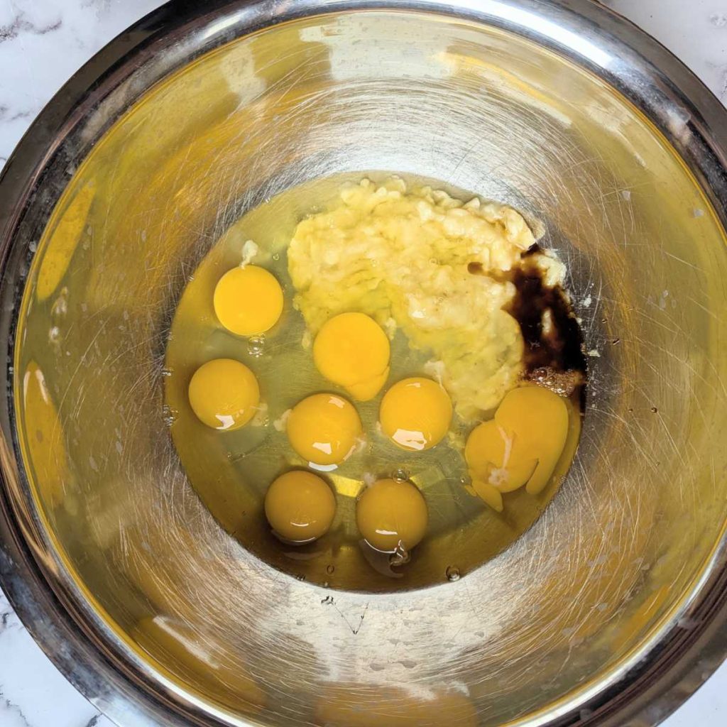mashed banana cracked eggs, and vanilla in a mixing bowl