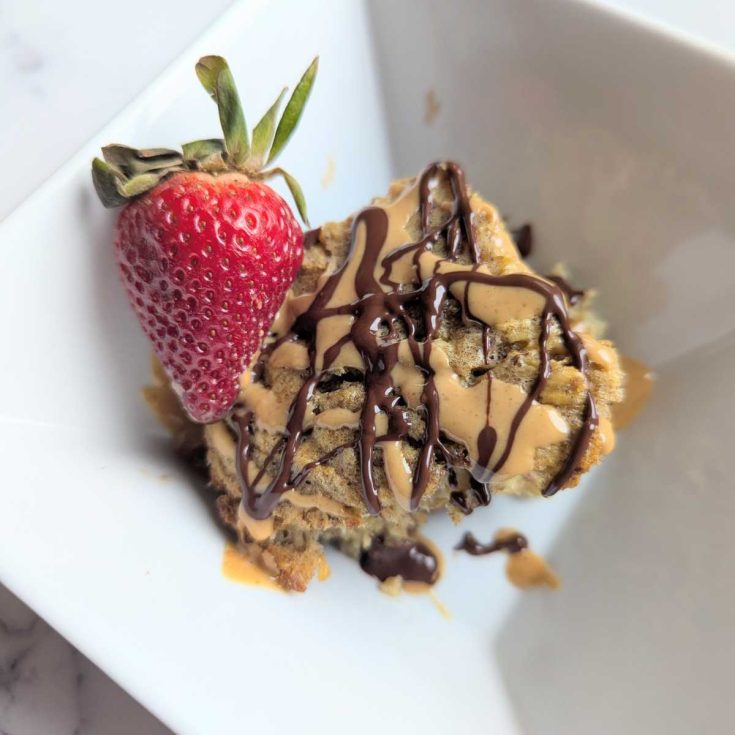 baked protein oats in bowl with peanut butter and chocolate drizzle with a strawberry on the side
